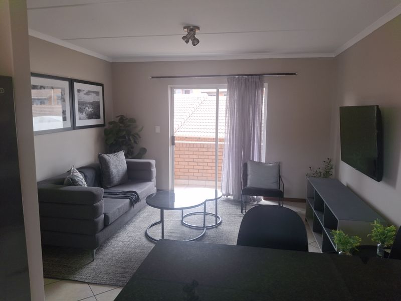 A well-maintained living room featuring tiled flooring, a ceiling spotlight fixture, and a sliding glass door providing access to an outdoor balcony area.