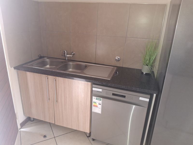 Compact kitchen area featuring a stainless steel double sink, granite countertop, tiled splashback, and built-in cabinetry with an integrated dishwasher.
