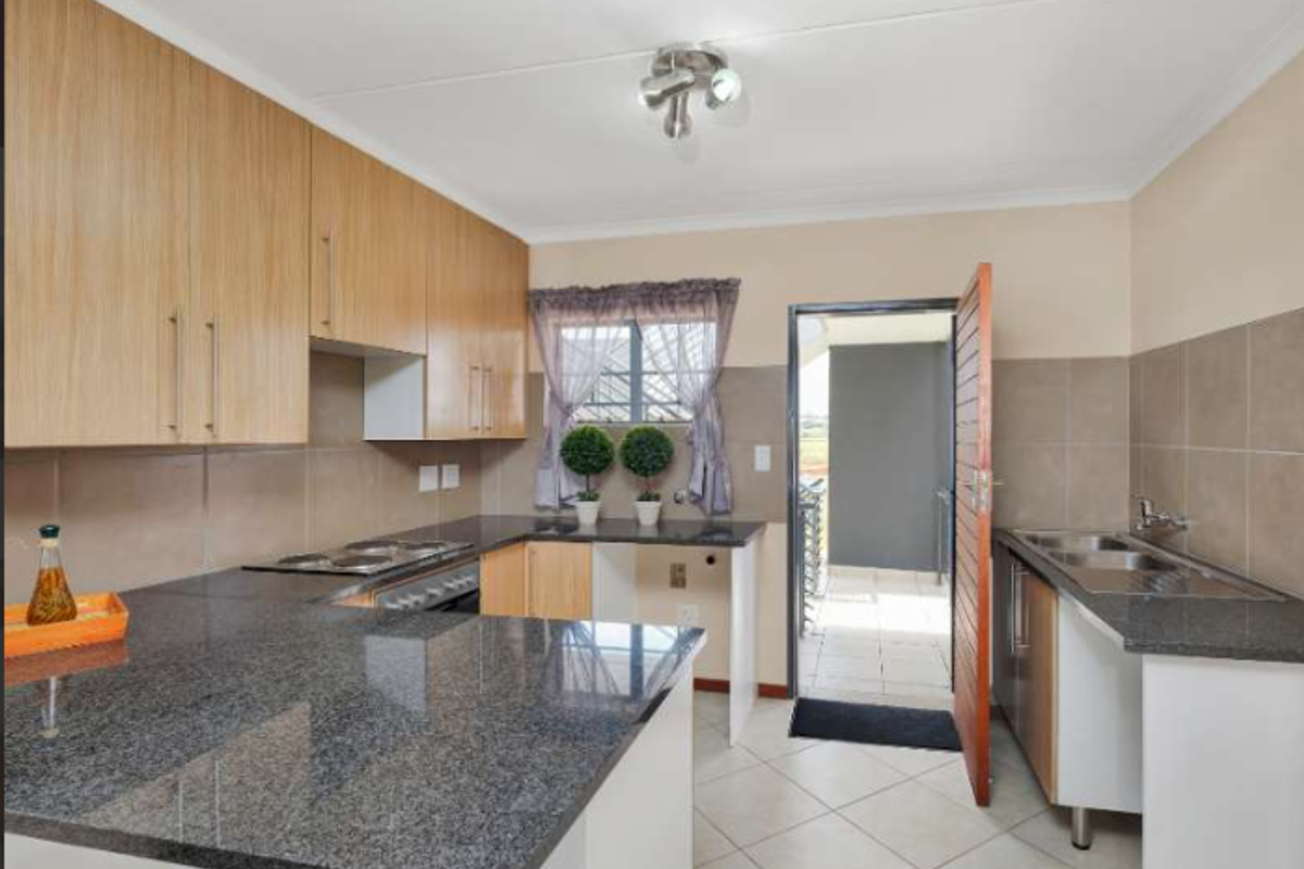 A functional kitchen featuring granite countertops, built-in wooden cabinetry, an electric hob, and a double basin sink with direct access to an outdoor area.