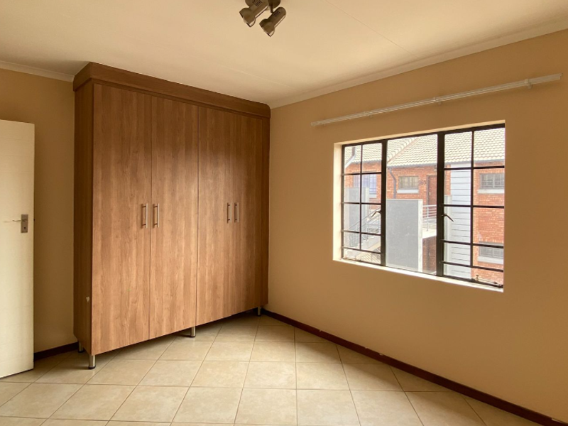 A clean, empty bedroom featuring neutral walls, tiled flooring, and a large built-in wooden wardrobe with ample storage space.