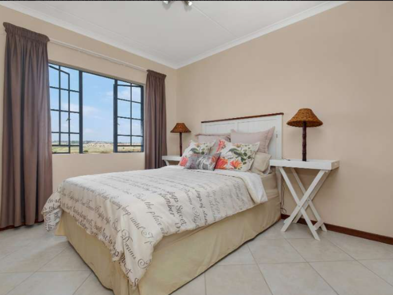 A well-maintained bedroom featuring neutral wall tones, tiled flooring, and a large casement window providing natural light and exterior views.