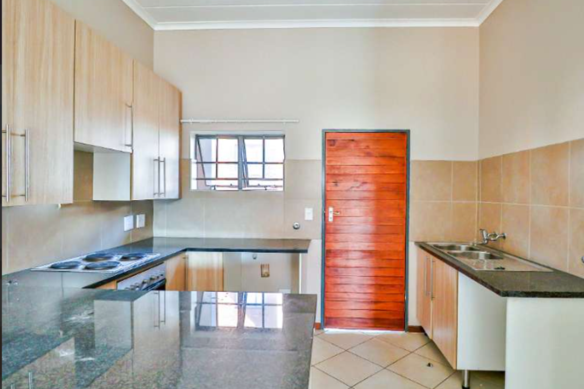 A functional kitchen featuring granite countertops, built-in cabinetry, an electric hob, oven, and a double basin sink with tiled backsplash and flooring.