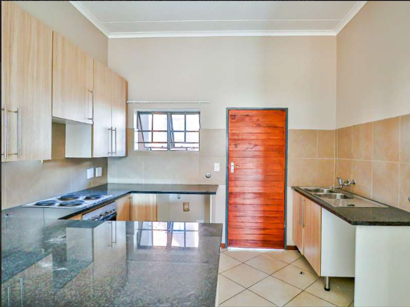 A functional kitchen featuring granite countertops, built-in cabinetry, an electric hob, oven, and a double basin sink with tiled backsplash and flooring.