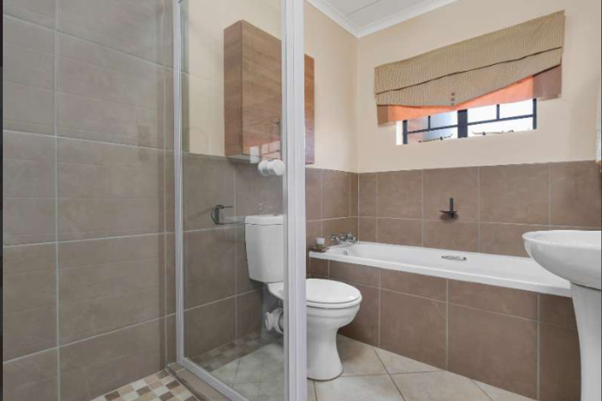 A functional bathroom featuring a shower enclosure, bathtub, pedestal basin, and toilet with neutral wall and floor tiling.