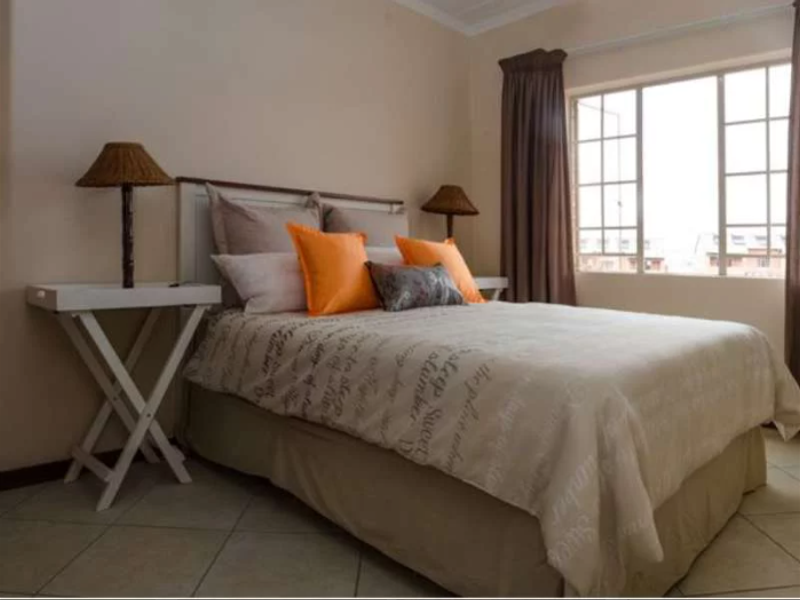 A well-lit bedroom featuring neutral tiled flooring and a large window with curtain tracks, providing a comfortable and functional living space.