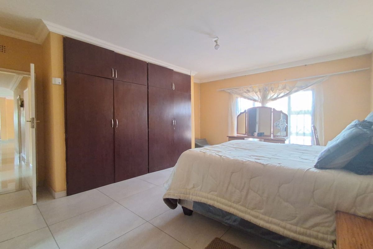 A spacious bedroom featuring large built-in wooden cupboards, tiled flooring, and natural light from a window.