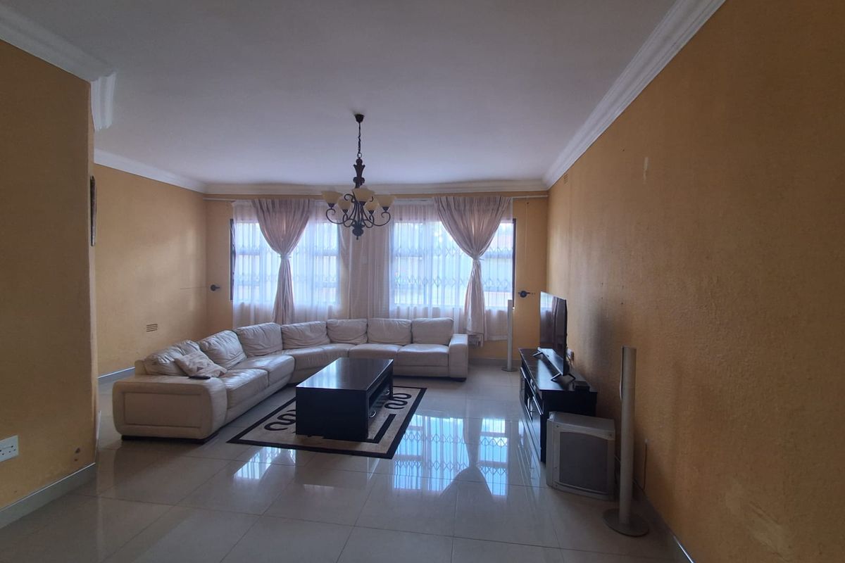Spacious living room featuring tiled flooring, decorative ceiling cornices, and a central chandelier, providing a comfortable and functional family living area.