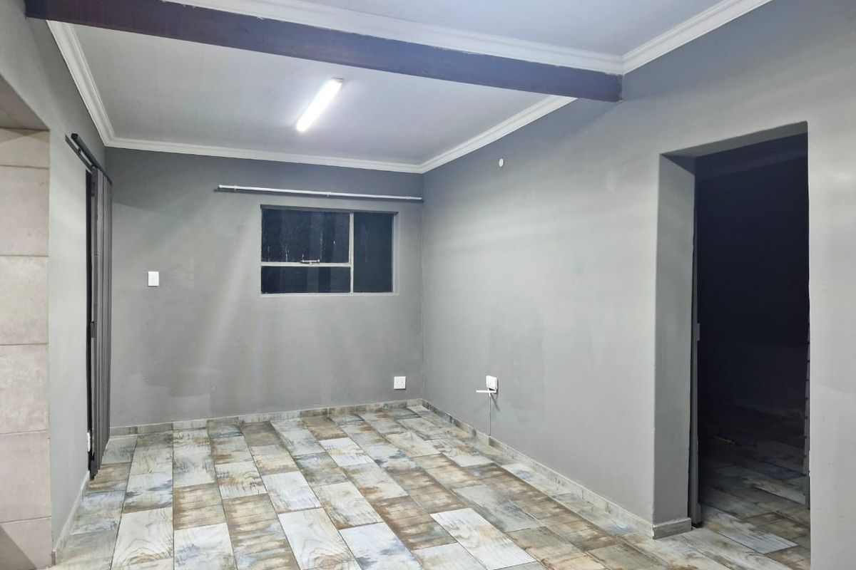 An empty living room featuring grey painted walls, tiled flooring, and a prominent exposed ceiling beam.