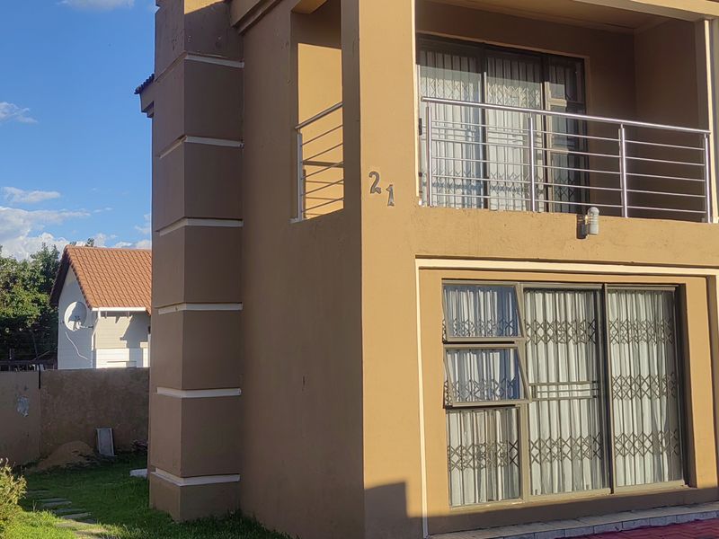 Front elevation of a two-story residential property featuring a balcony with stainless steel balustrades, sliding doors with security gates, and a paved driveway.