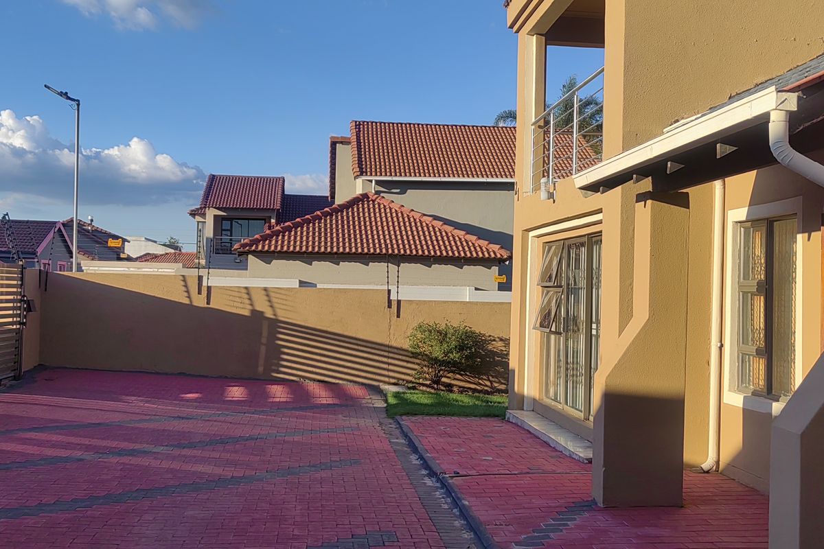 Rear exterior view showing a paved driveway, boundary wall with electric fencing, and access to the main dwelling via sliding glass doors.