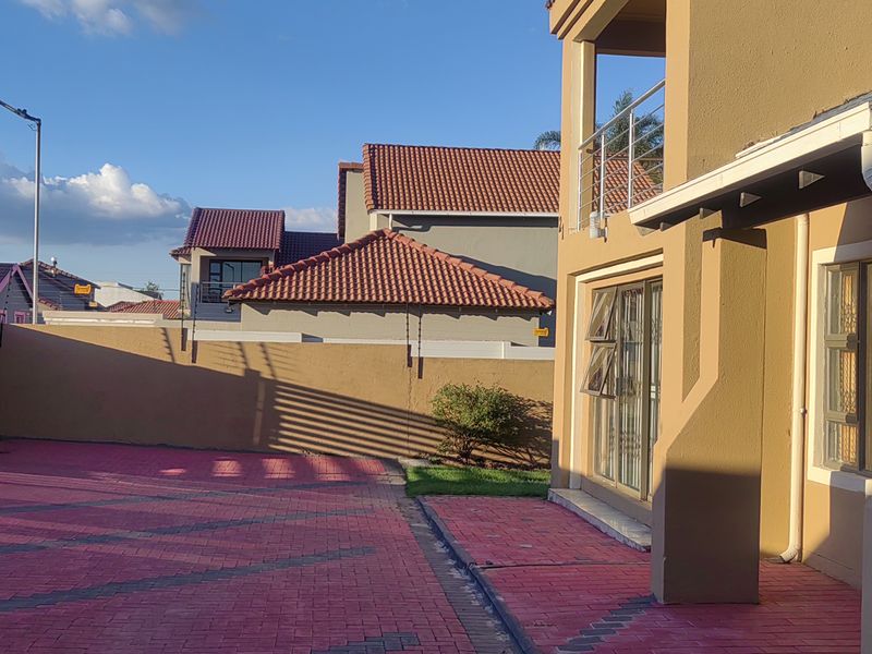 Rear exterior view showing a paved driveway, boundary wall with electric fencing, and access to the main dwelling via sliding glass doors.