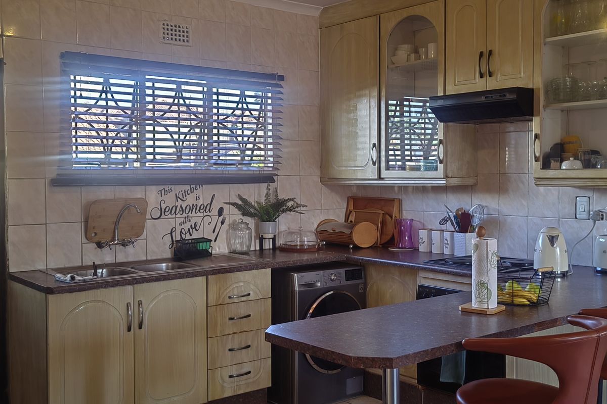 A functional kitchen featuring built-in cabinetry, laminate countertops, a double sink, and integrated laundry plumbing, with a tiled backsplash and extractor fan.