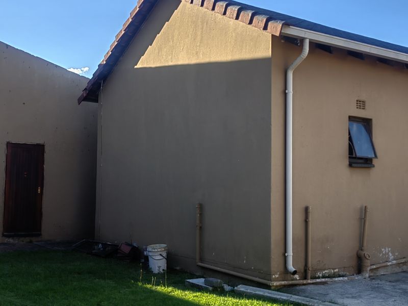 Rear view of the property showing plastered exterior walls, tiled roofing, and external plumbing fixtures with some visible wear to the base finishes.