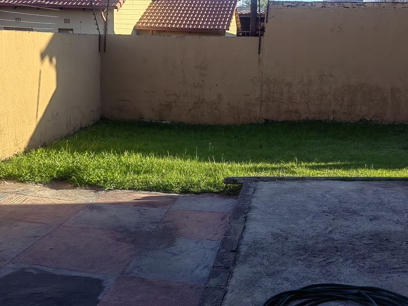 A private rear garden area featuring a paved patio, a small lawn, and high boundary walls, offering potential for outdoor landscaping and improvement.