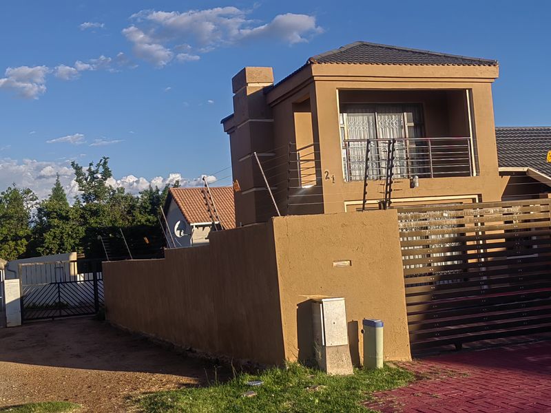 Front exterior view of a two-story residential property featuring a paved driveway, sliding gate, and balcony with electric fencing.