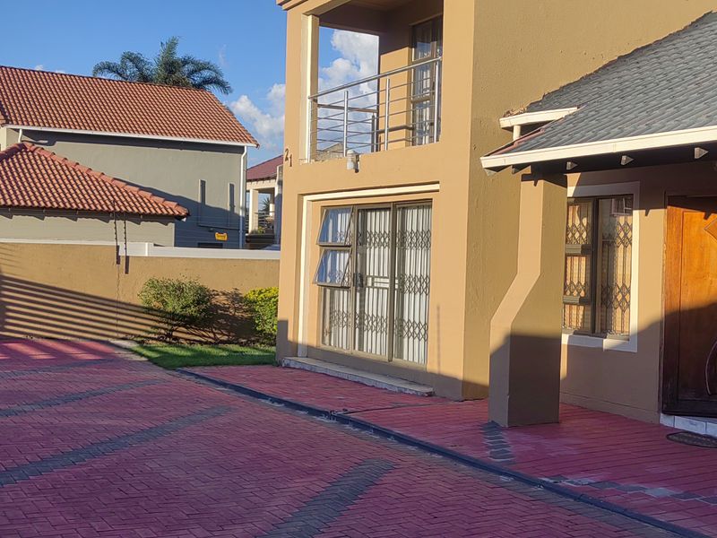 Front elevation of a two-story residential property featuring a paved driveway, timber entrance door, and an upper-level balcony with stainless steel railings.