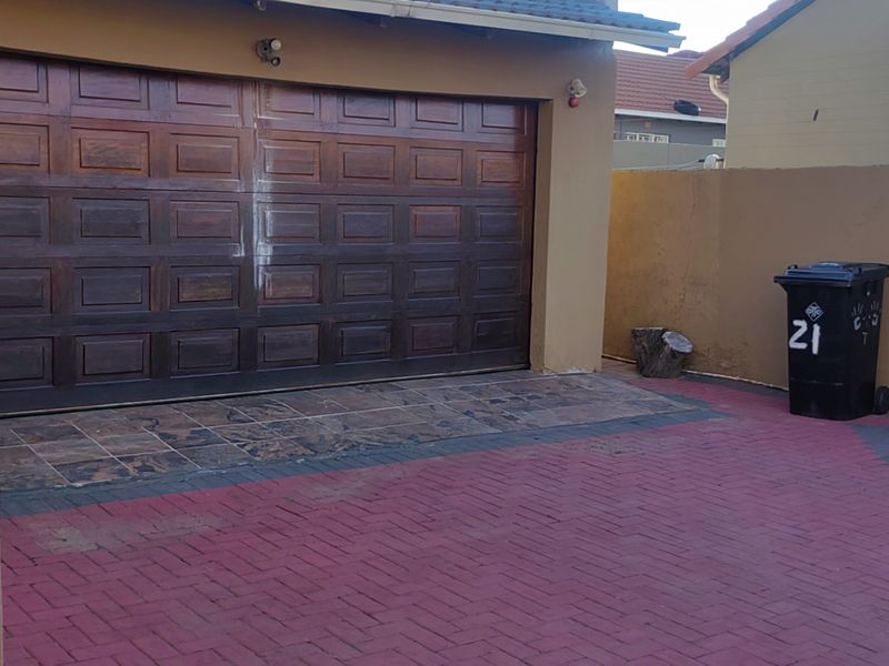 A paved driveway leading to a double garage with a wooden sectional door, enclosed by a boundary wall.