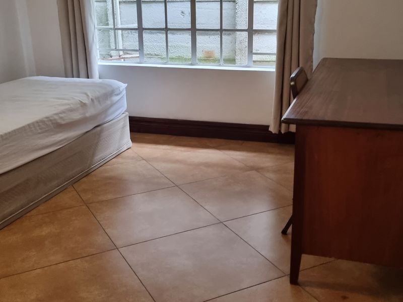 A functional bedroom featuring tiled flooring and a window fitted with security bars, providing a simple and practical living space.