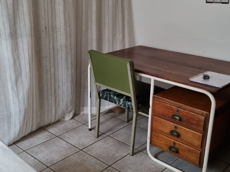 A bedroom space featuring tiled flooring and a wooden door frame, offering a functional area for a home office or sleeping quarters.