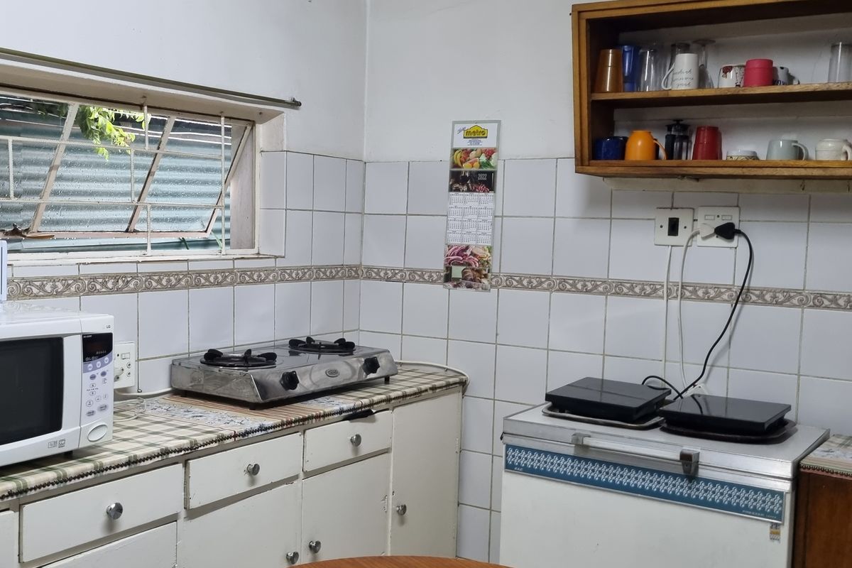 A functional kitchen area featuring tiled walls, built-in cabinetry, and wall-mounted shelving, offering a practical layout with potential for modern updates.