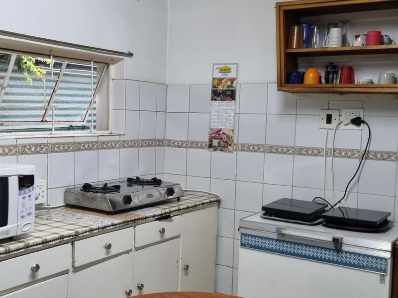 A functional kitchen area featuring tiled walls, built-in cabinetry, and wall-mounted shelving, offering a practical layout with potential for modern updates.