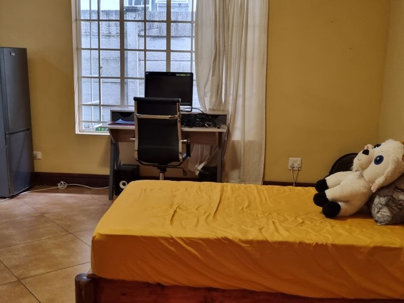 A bedroom featuring tiled flooring and large windows with security bars, providing natural light and a functional layout.