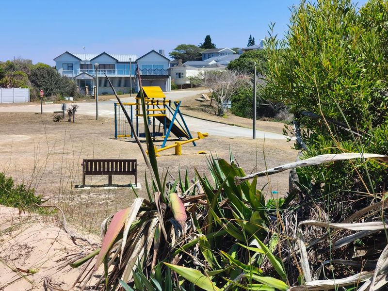 A view of a communal garden area featuring a playground, park bench, and paved access road within a residential estate.