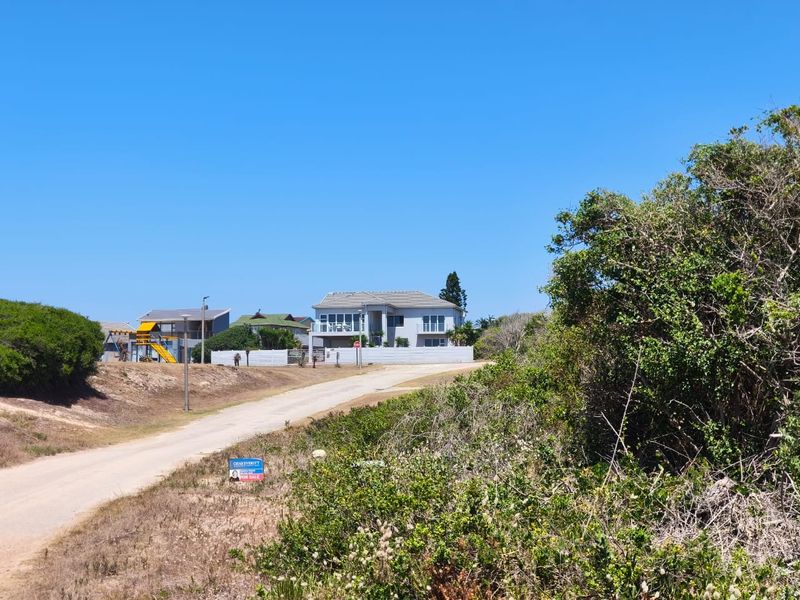 A street-level view of a residential property and surrounding vacant land, showcasing the neighborhood approach and access road.