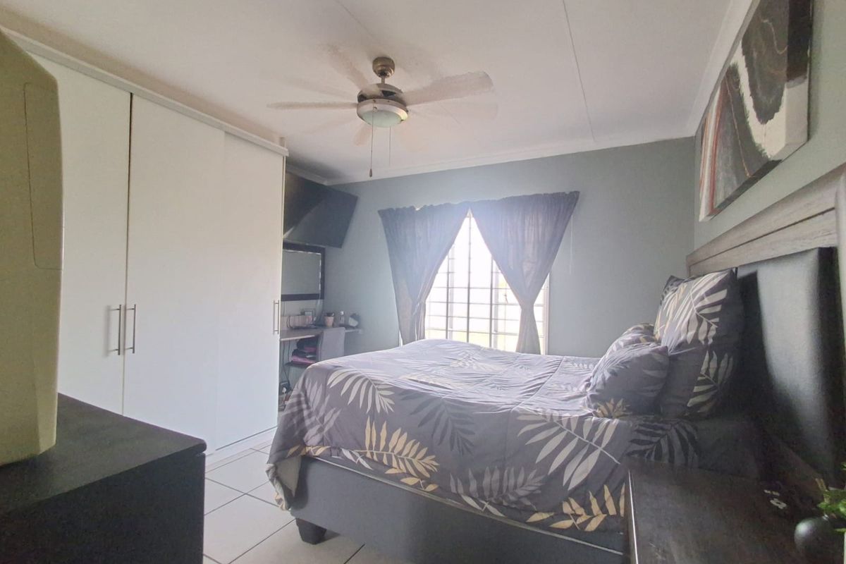 A functional bedroom featuring built-in sliding door wardrobes, tiled flooring, and a ceiling fan, offering a comfortable and practical living space.