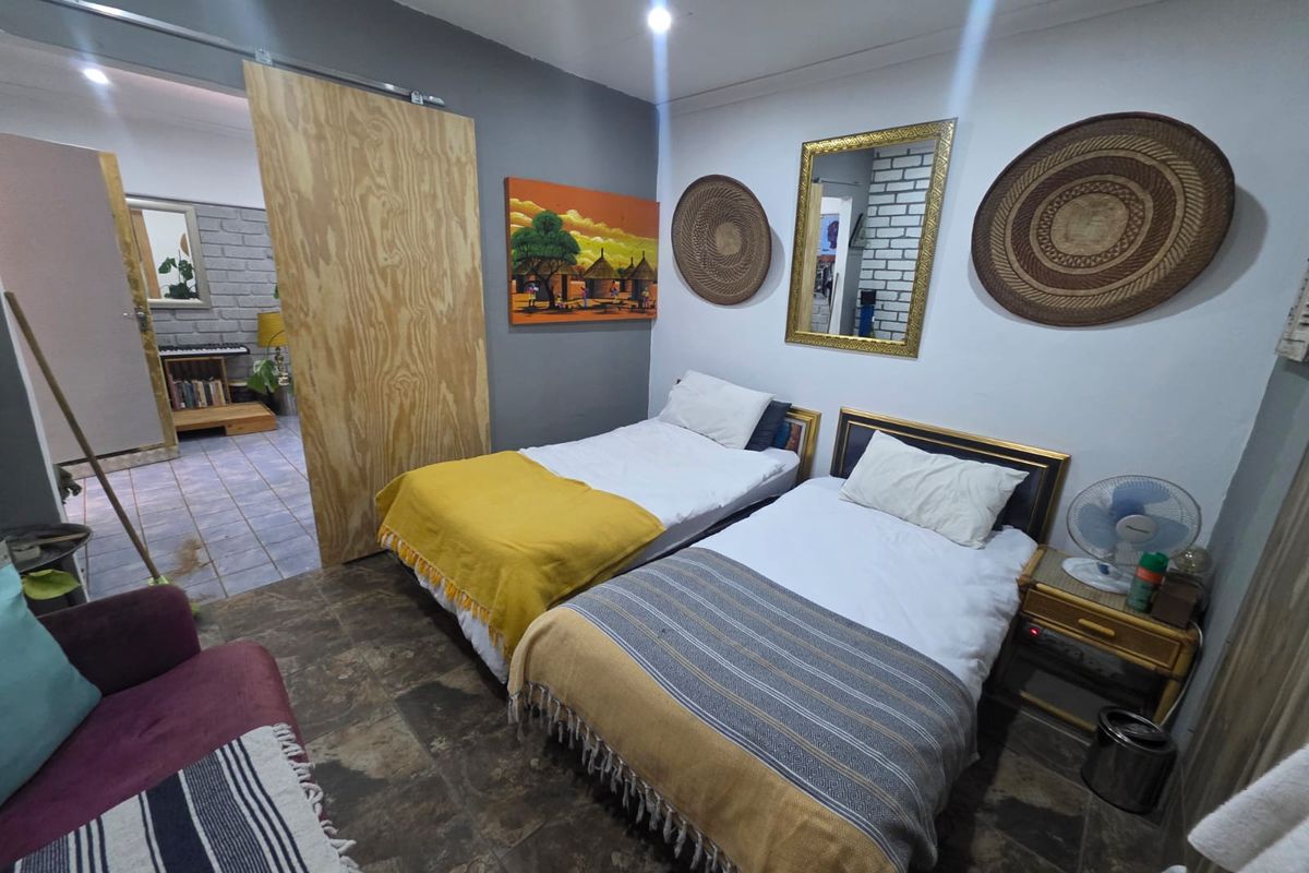 A bedroom featuring tiled flooring, a sliding plywood door, and access to an adjacent room with exposed brickwork.