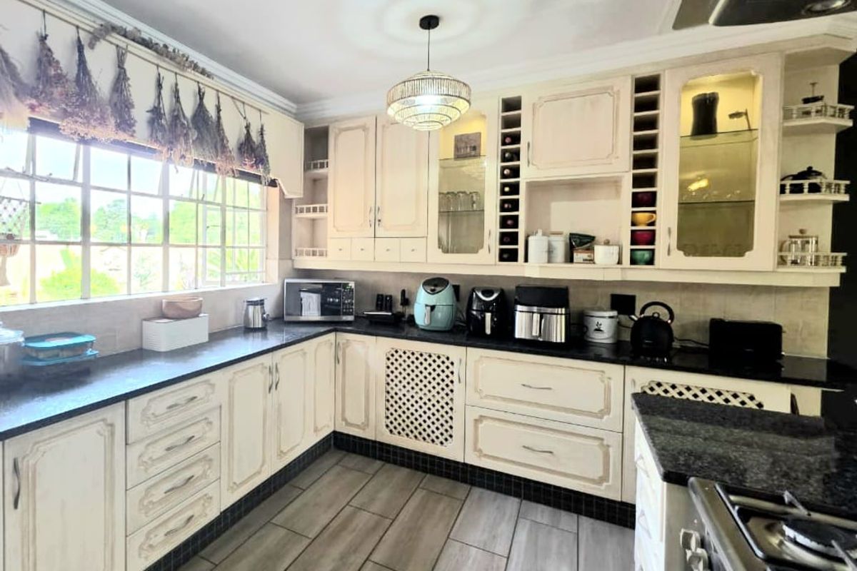 A functional kitchen featuring cream-toned cabinetry, dark granite countertops, tiled flooring, and a large window providing natural light.