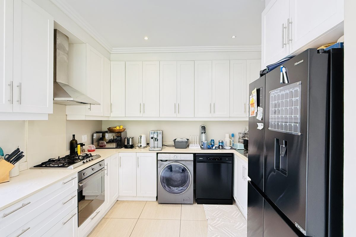 Modern kitchen featuring white cabinetry, integrated stainless steel oven, gas hob, extractor fan, and built-in laundry and dishwasher appliances.