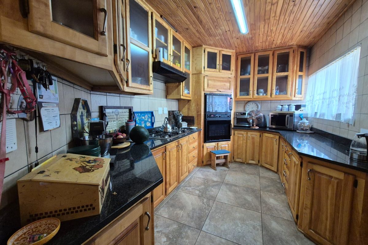 A traditional kitchen featuring extensive timber cabinetry, dark granite countertops, tiled flooring, and a wood-paneled ceiling with integrated built-in oven and hob.