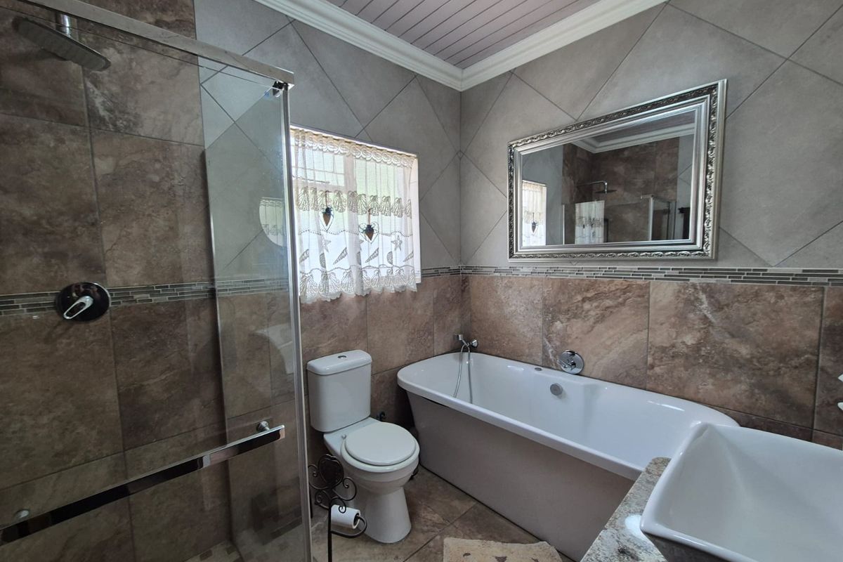 A well-appointed bathroom featuring a glass-enclosed shower, a freestanding bathtub, a toilet, and a vanity with a basin, finished with neutral wall tiling.