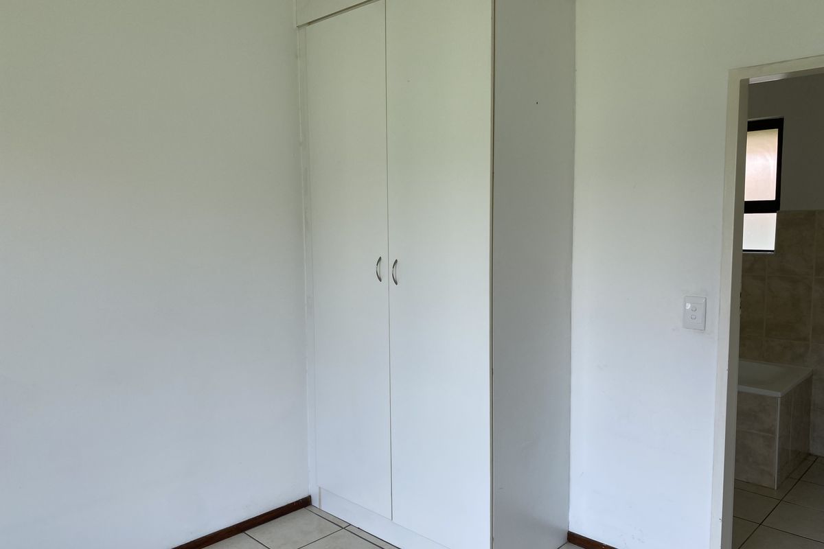 A clean, empty bedroom featuring white built-in wardrobes, neutral tiled flooring, and direct access to an adjoining bathroom.