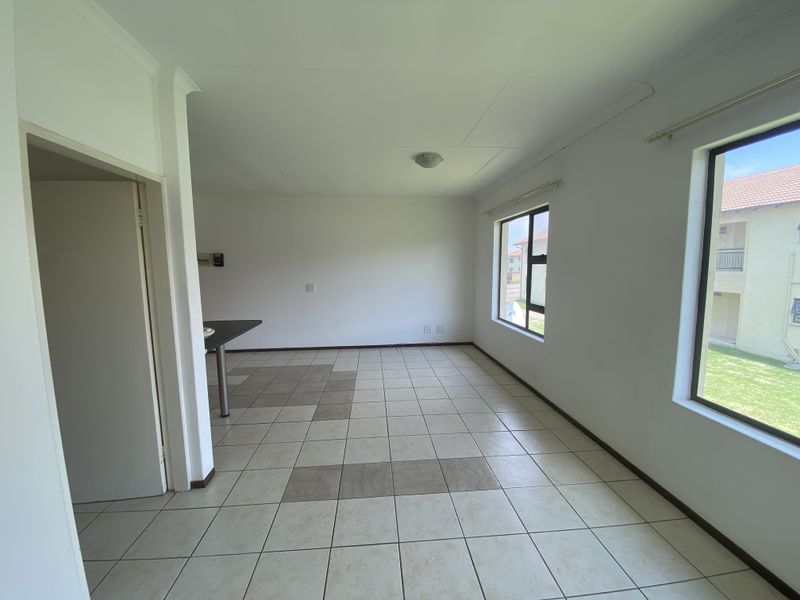 A bright and spacious open-plan living area featuring neutral tiled flooring, large windows for natural light, and a built-in breakfast bar.