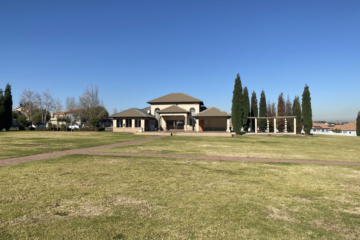 A wide-angle view of the rear exterior of the townhouse, featuring a large manicured lawn, paved pathways, and a covered pergola structure.