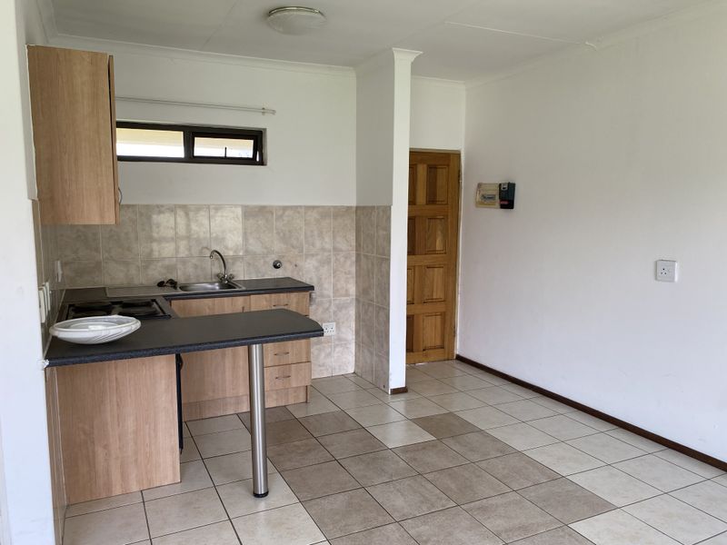 A functional kitchen area featuring laminate cabinetry, a built-in hob, tiled backsplash, and ceramic flooring, presenting a clean, empty space ready for updates.