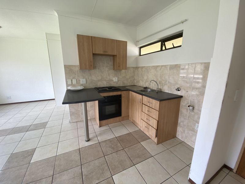 A functional kitchen featuring light wood cabinetry, laminate countertops, a built-in oven and hob, and tiled flooring in an open-plan layout.