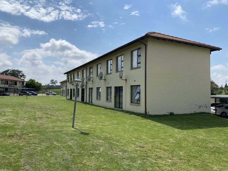 Exterior view of a multi-unit townhouse complex featuring plastered walls, tiled roofing, and communal lawn space.