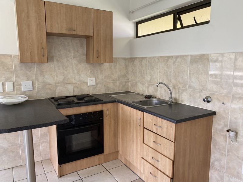 A compact kitchen featuring laminate cabinetry, built-in electric oven and hob, tiled backsplash, and a stainless steel sink.