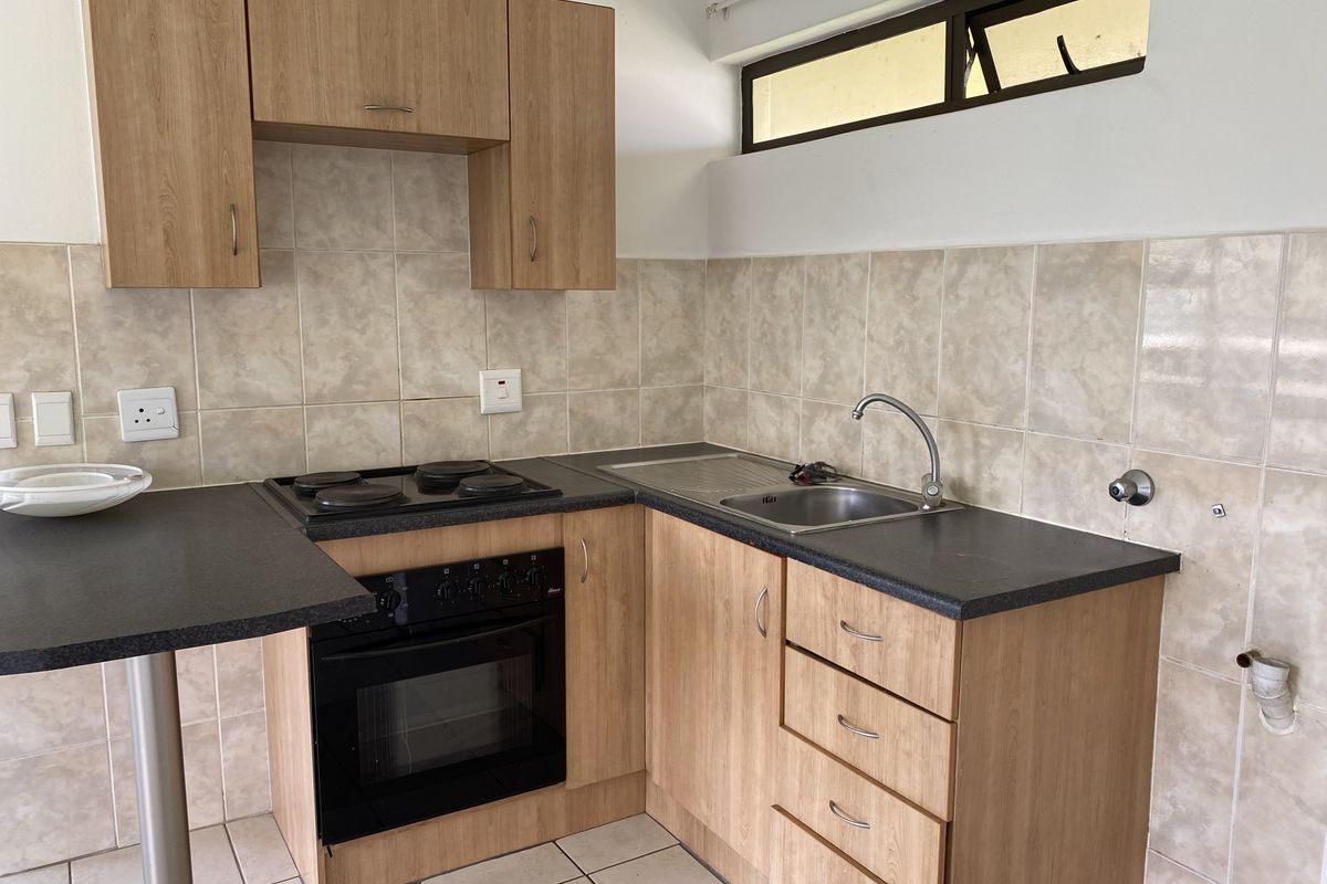 A compact kitchen featuring laminate cabinetry, built-in electric oven and hob, tiled backsplash, and a stainless steel sink.
