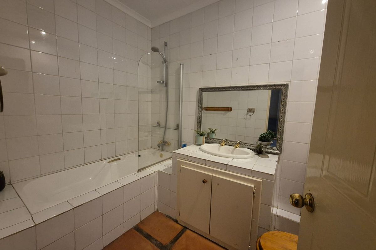 A dated bathroom featuring a tiled bathtub with glass screen, a built-in vanity with basin, and terracotta floor tiles.