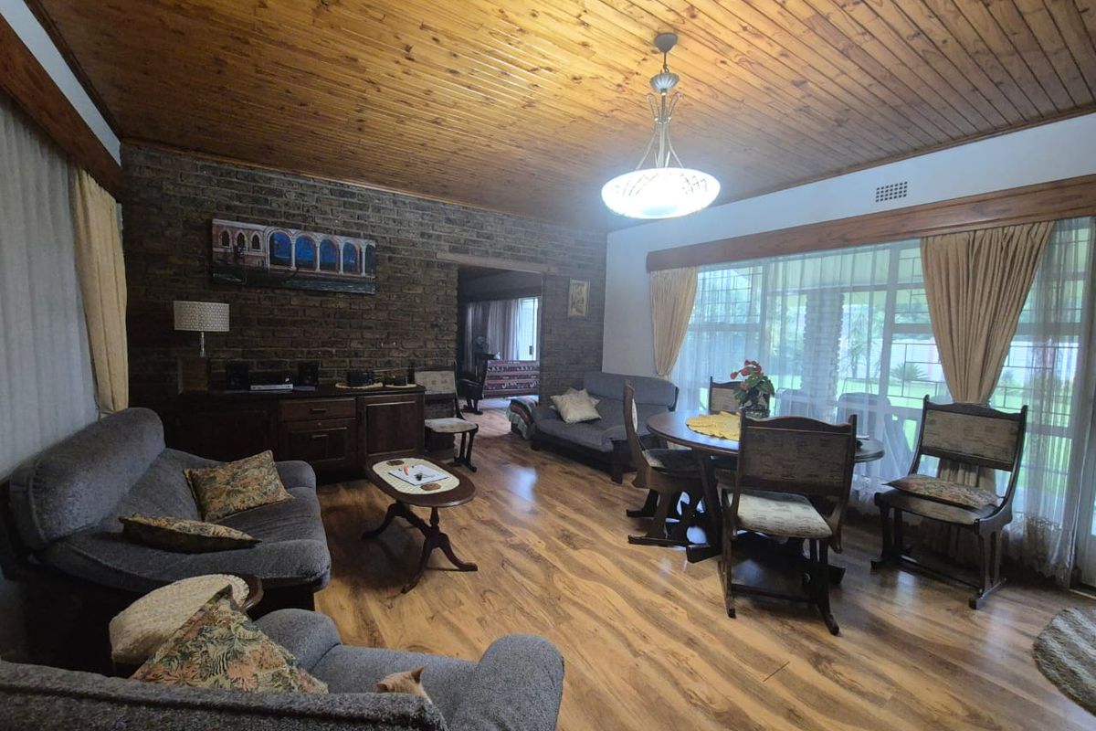 Spacious living room featuring exposed brick walls, a warm timber-paneled ceiling, and durable laminate flooring with large windows providing natural light.