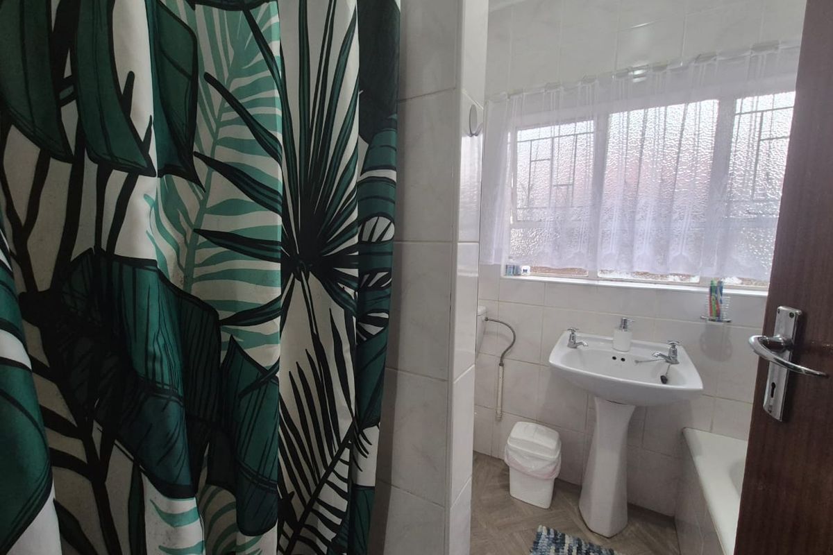 A functional bathroom featuring a pedestal basin, bathtub, and tiled wall finishes, with natural light provided by a window with security bars.