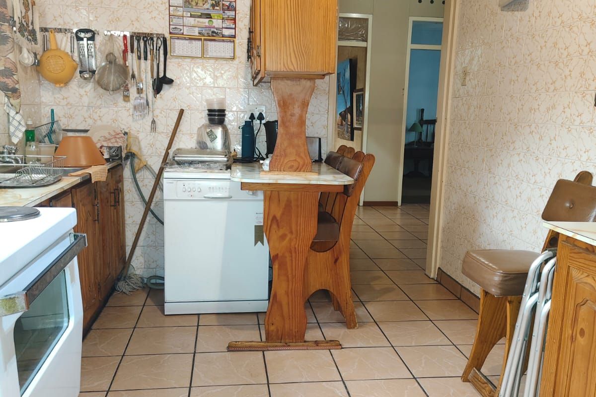 A dated kitchen featuring tiled walls, wooden cabinetry, and tiled flooring, with a functional layout and direct access to the hallway.