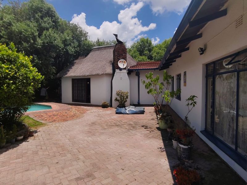 A spacious rear courtyard featuring brick paving, a thatched roof structure, and access to a swimming pool area.