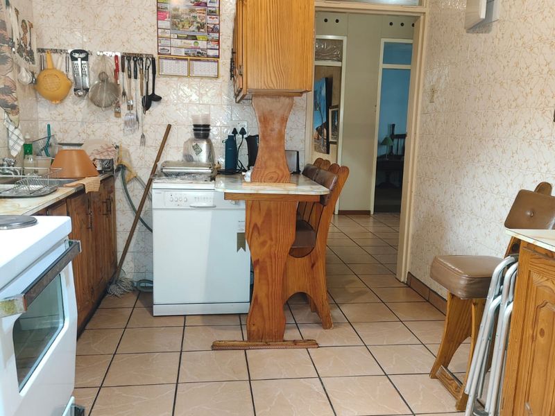 A dated kitchen featuring tiled walls, wooden cabinetry, and tiled flooring, with a functional layout and direct access to the hallway.