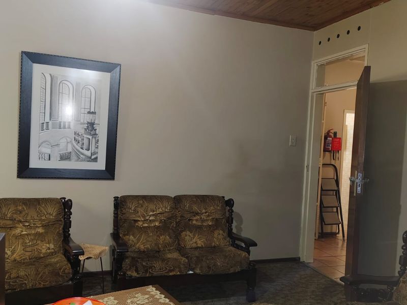 A living room featuring a timber-paneled ceiling and carpeted flooring, with an open doorway leading to an adjacent utility area.