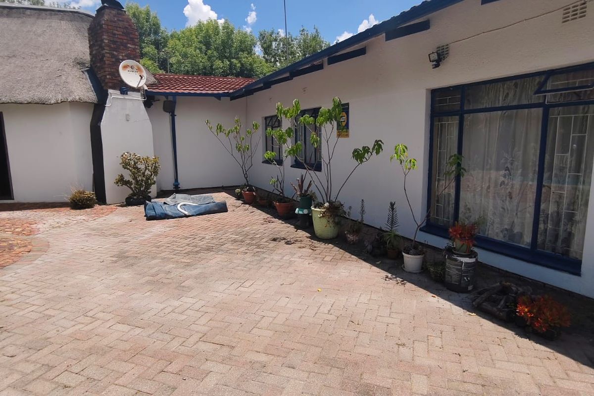 A paved rear courtyard area featuring a brick chimney, thatched roof section, and large windows, providing a functional outdoor space.